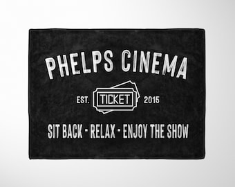 May include: Black and white sign with the text "Phelps Cinema" and "Est. 2015" with a ticket icon. The text "Sit back - Relax - Enjoy the show" is below the main text.