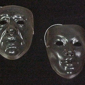 May include: Two black plastic masquerade masks. One mask has a serious expression with furrowed brows and a downturned mouth. The other mask has a more neutral expression with a slightly open mouth.