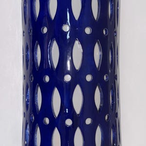 May include: A cylindrical wall sconce featuring a deep cobalt blue glazed ceramic finish. The surface is adorned with a repeating pattern of vertical almond-shaped cutouts interspersed with small circular perforations throughout the body.