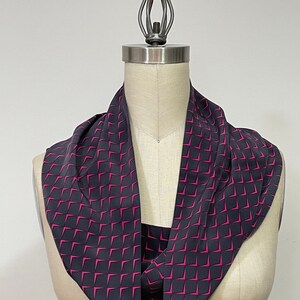 May include: A black and pink patterned infinity scarf. The scarf is made of a soft, silky fabric and has a geometric design.