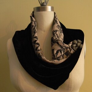 May include: A black velvet scarf with a beige and black patterned scarf layered on top. A silver brooch with a flower design is pinned to the scarf.