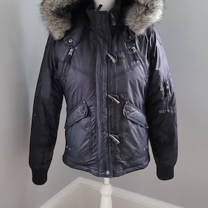 May include: A black puffer jacket with a faux fur hood. The jacket has a zipper closure and toggle buttons.