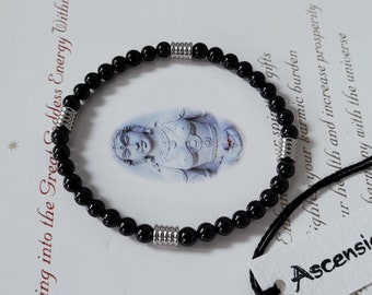 Puede incluir: Pulsera de cuentas negras con detalles plateados. La pulsera está sobre una superficie blanca con texto que dice "bringing into the Great Goddess Energy Within" y "Ascensi".