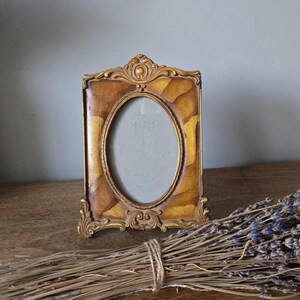 May include: A gold-toned oval picture frame with ornate detailing. The frame has a wood-grain pattern and a slightly distressed finish.