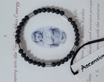 Puede incluir: Pulsera de cuentas de roca volcánica negra con detalles de metal plateado. La pulsera está sobre un fondo blanco con texto que dice "Tapping into the Grey Goddess Energy With" e "Imp. Ascension".
