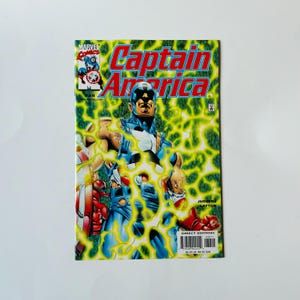 May include: A comic book cover for Captain America, featuring the superhero in a blue and white costume with a shield. The cover has a green and yellow background with the title "Captain America" in red and blue.