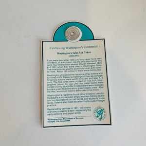 May include: A close-up of a green and white card with a small aluminum token attached. The card reads "Celebrating Washington's Centennial" and "Washington's Sales Tax Token (1935-1951)". The text explains the history of the token and its use in Washington State.