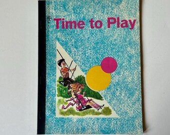May include: A softcover book titled Time to Play with a light blue textured background. The cover features a triangular illustration of two children on swings over green grass, alongside a large yellow circle and a smaller pink circle.
