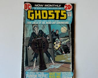 May include: A vintage DC comic book titled Ghosts No. 9, dated November. The cover features a skeleton in a captain's uniform steering a ship, with two men nearby. Text includes Now Monthly, 20c, and Curse of the Phantom Prophet.