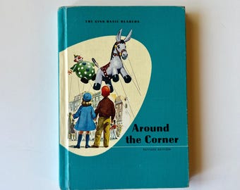 May include: A teal hardcover book titled The Ginn Basic Readers Around the Corner Revised Edition. The cover features an illustration of a child in a blue coat and a child in a brown shirt looking up at a marionette donkey and a clown puppet.