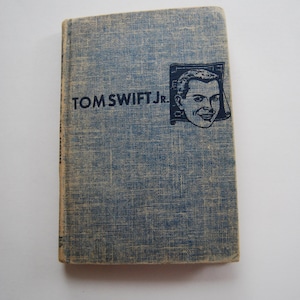 May include: A blue book with the text "TOM SWIFT JR." on the cover. The cover also features a black and white illustration of a man's face.