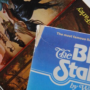May include: A blue paperback book with the title "The Black Stallion" by Walter Farley. The book cover features a white stylized font and the text "The most famous file" is printed in black.