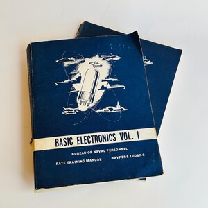 May include: A blue book titled "Basic Electronics Vol. 1" with a white illustration of a vacuum tube and airplanes. The book is a Rate Training Manual for the Bureau of Naval Personnel, NAVPERS 10087-C.