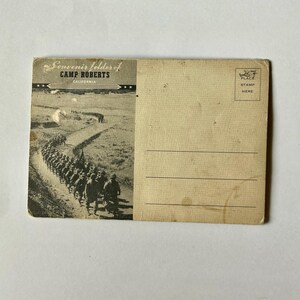 May include: Vintage postcard with a black and white image of soldiers marching on a dirt road. The postcard is labeled "Souvenir folder of Camp Roberts California" with a stamp area and lines for writing.