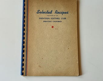 May include: A tan spiral-bound cookbook titled Selected Recipes Published by the Saratoga Foothill Club Saratoga, California. The cover features a blue plastic coil binding, a red and blue vertical line, and a small red square logo with an S.
