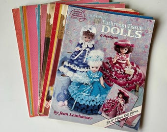 May include: A stack of craft pattern booklets featuring a primary guide titled Crocheted Bathroom Tissue Dolls by Jean Leinhauser. The cover displays three dolls in blue, teal, and magenta crocheted dresses, with text for 8 inch pillow doll forms.