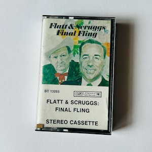 May include: A vintage cassette tape for "Flatt & Scruggs: Final Fling." The cassette features a color image of two men and the album title. The tape is labeled "Stereo Cassette" and includes the CBS Records logo.