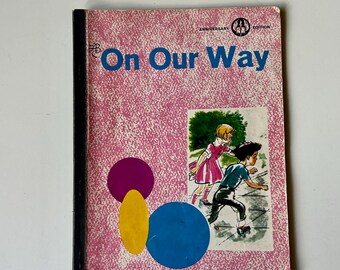May include: A vintage book titled On Our Way Anniversary Edition with a pink textured cover. The front features a black spine, a purple circle, a yellow oval, a blue circle, and an illustration of a child in a pink dress and a child on roller skates.
