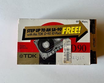 May include: A TDK D-90 10-pack cassette tape box featuring a red, white, and gold design. The packaging includes a large gold arrow graphic with the text STEP UP TO AN SA-90 FREE! and a barcode sticker with the price 12.99 printed on it.
