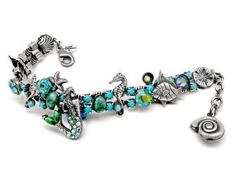May include: A silver bracelet with a mermaid, seahorse, and fish charms. The charms are decorated with turquoise and green crystals. The bracelet has a silver clasp and a silver shell charm.