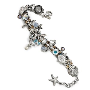 May include: A silver charm bracelet with a nautical theme. The bracelet features charms of seahorses, starfish, seashells, fish, and a dragonfly. The charms are adorned with blue, white, and brown crystals.