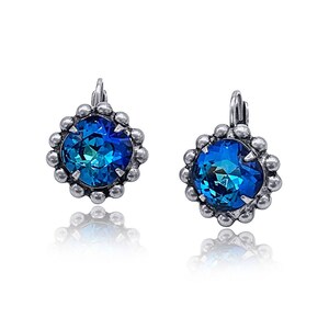 May include: A pair of silver earrings with a blue crystal in the center of each earring. The crystals are surrounded by a silver beaded halo.