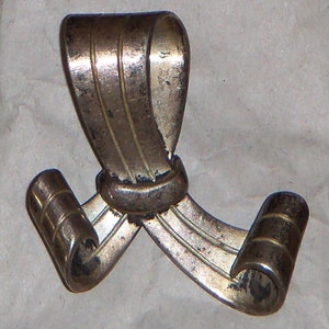 May include: A silver-toned metal bow tie with a decorative design. The bow tie is tied in a knot and has a loop at the top for hanging.