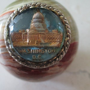 May include: A small, round, multi-colored marble with a silver-rimmed, blue glass inset featuring a gold image of the US Capitol building and the text "WASHINGTON D.C."