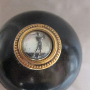 May include: A black round knob with a gold-rimmed circular inset featuring a black and white image of a person playing golf.
