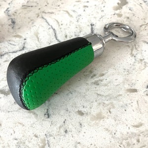 May include: A black and green bottle opener with a leather handle. The handle is textured and has a black stitching detail.