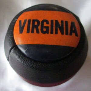 May include: A black leather gear shift knob with an orange and black stripe design. The knob has the word "VIRGINIA" printed in black letters on the orange stripe.