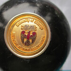 May include: A gold-colored pin with the text "University of Chicago Medical Alumni Association" and a red and gold eagle emblem.