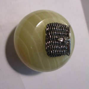 May include: A small, round, green and white marble paperweight with a silver metal basket on top.