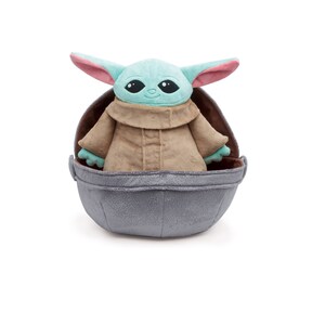 May include: A plush toy of the character "The Child" from the Star Wars series, known as "Baby Yoda", wearing a brown robe and sitting in a gray egg-shaped pod.