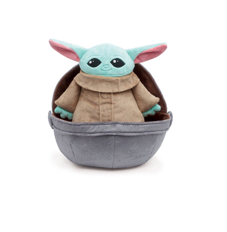 May include: A plush toy of the character "The Child" from the Star Wars series, known as "Baby Yoda", wearing a brown robe and sitting in a gray egg-shaped pod.