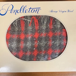 May include: A Pendleton blanket in a cream-colored box. The blanket has a red, gray, and black plaid pattern. The box has the Pendleton logo and the words "Always Virgin Wool".