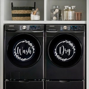May include: Black washer and dryer with a white wreath design on the front of each appliance. The washer says "Wash" and the dryer says "Dry".