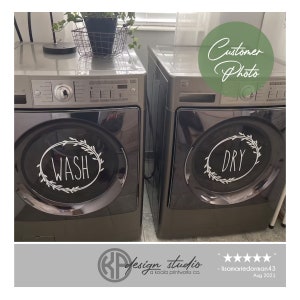 May include: Two black washing machines with white vinyl decals on the front. The decals are in the shape of a wreath with the words "WASH" and "DRY" inside.
