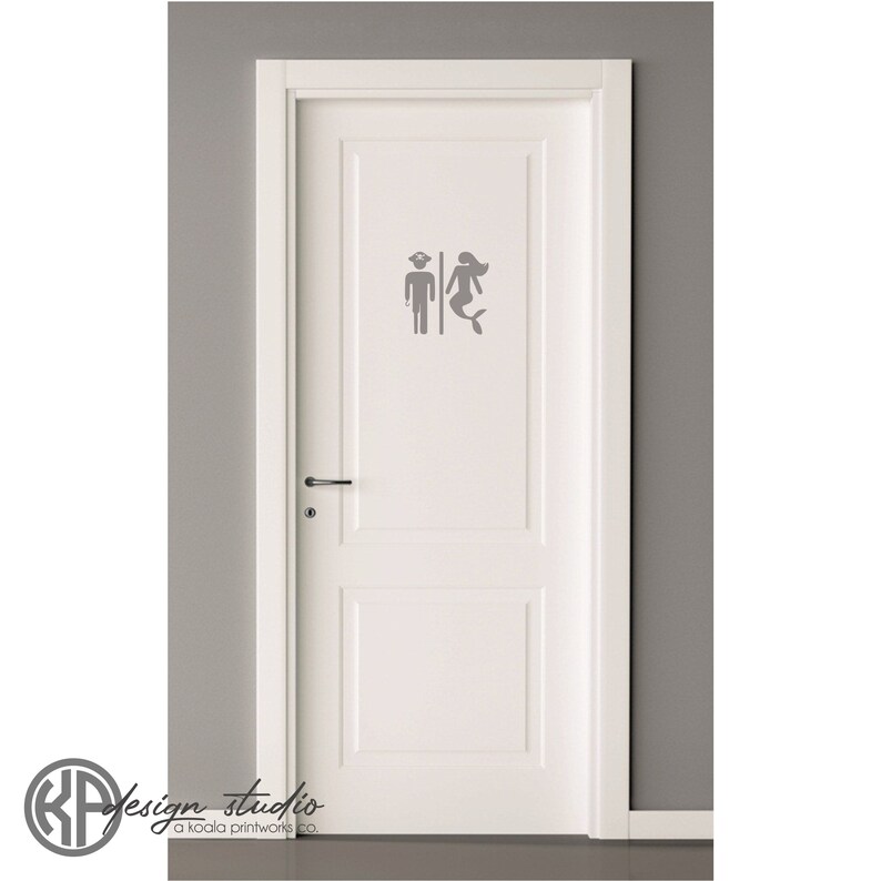 May include: A white door with a gray vinyl decal of a mermaid and a man with a captain's hat. The decal is a bathroom sign.