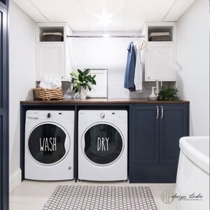 May include: A white washer and dryer with the words "WASH" and "DRY" on the front. The appliances are in a laundry room with dark blue cabinets and a wood countertop.