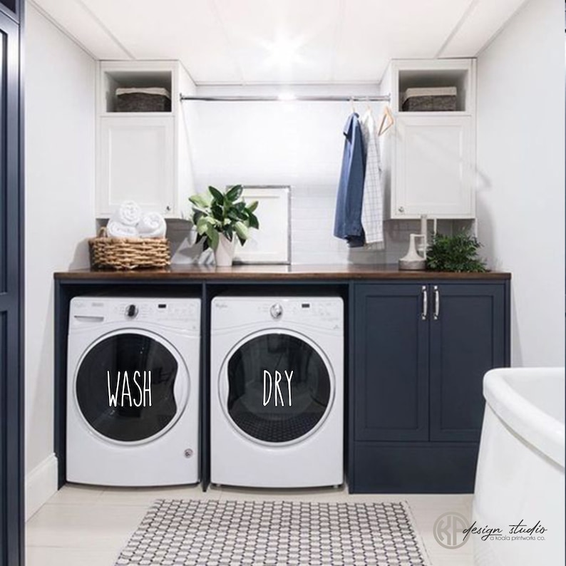 May include: A white washer and dryer with the words "WASH" and "DRY" on the front. The appliances are in a laundry room with dark blue cabinets and a wood countertop.
