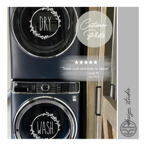 May include: A set of two white vinyl decals for a washer and dryer. The decals feature a wreath design with the words "WASH" and "DRY" in black script font. The decals are shown on a dark blue washer and dryer.