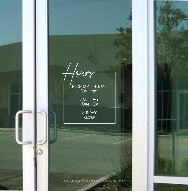 May include: A white sign with black text on a glass door, displaying business hours. The sign reads: "Hours. Monday - Friday 9AM - 6PM. Saturday 10AM - 2PM. Sunday Closed."