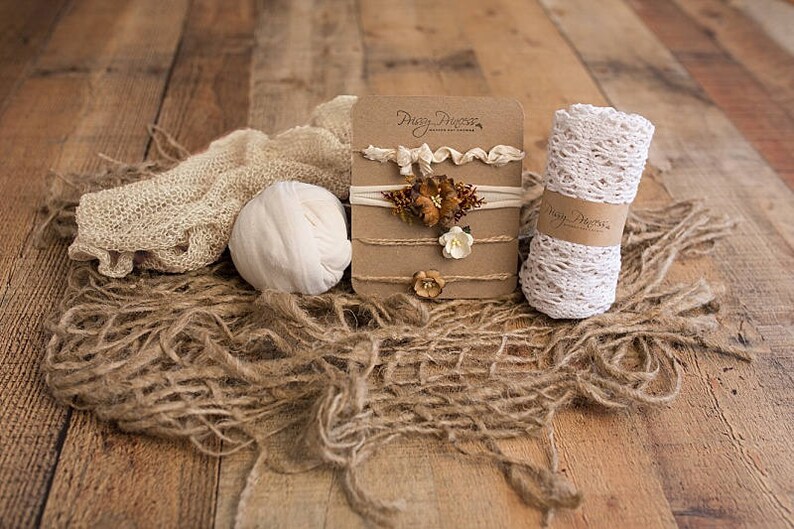 May include: Three brown cardboard cards with the text "Pretty Pieces" on the top card. Each card features a different floral headband with white and brown accents. The cards are displayed on a rustic wooden surface with a white crocheted headband, a white knitted ball, and a brown burlap fabric.