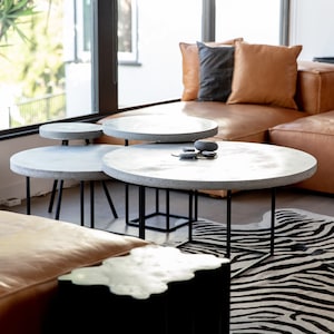 May include: A living room with a brown leather sectional sofa, a zebra print rug, and a set of round concrete coffee tables with black metal legs.