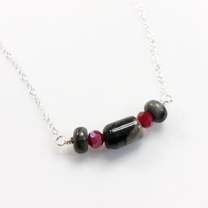 May include: A silver chain necklace with a black and grey stone and red glass beads.