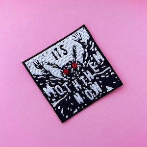 Op de afbeelding: Zwarte en witte geborduurde patch met een mottenmotief en de tekst "It is moth them now."