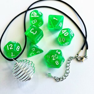 May include: A green and silver necklace with a wire cage pendant and six green dice with white numbers. The dice are a d4, d6, d8, d10, d12, and d20.