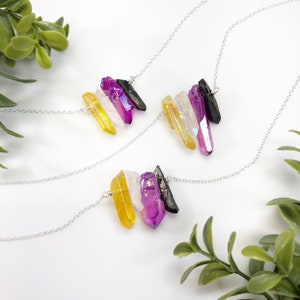 May include: Three necklaces featuring silver-toned chains and pendants composed of four raw crystal points in yellow, clear, magenta, and black. The crystals are arranged horizontally and attached to the delicate metal chain links.