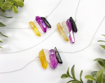 Könnte beinhalten: Drei Halsketten mit silberfarbenen Ketten und Anhängern, die aus vier rohen Kristallspitzen in Gelb, Transparent, Magenta und Schwarz bestehen. Die Kristalle sind horizontal angeordnet und an den feinen Metallkettengliedern befestigt.